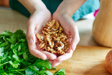 Walnuts in the hands of a woman against the background of a wooden table, cilantro greens. Chef's hands holding nuts without shells over the kitchen table for making sauces, dressings, desserts, sweet