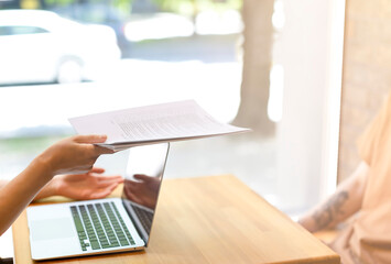 Interview, in the hands of a woman papers, a young man sits at a wooden table. A woman hands over documents to an employee in the office or in a bank. A man gets a job, a man signs documents