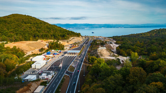 Aerial view of Učka (Ucka) Tunnel and toll booth surrounded on A8 motorway by autumn forest on the Rijeka side, showing colorful foliage and winding highway through the mountains