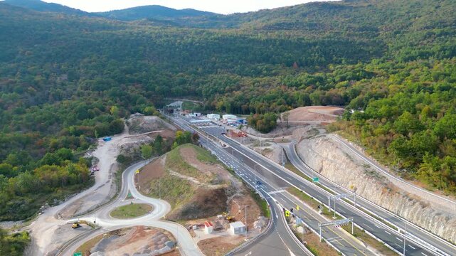Aerial view of Učka (Ucka) Tunnel and toll booth surrounded on A8 motorway by autumn forest on the Rijeka side, showing colorful foliage and winding highway through the mountains