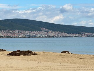 Sunny beach with calm blue sea and mountains in the distance. Coastal landscape in summer vacation mood.