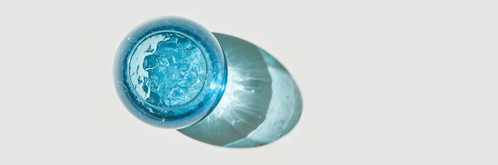 Top view of blue glass with water and ice casting shadow on white surface.