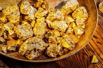 Gold nuggets on a brass plate on a wooden tabletop. Imitation gold nuggets.