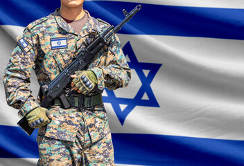 Obraz premium Israel flag with soldier in military uniform holding assault rifle in front of it