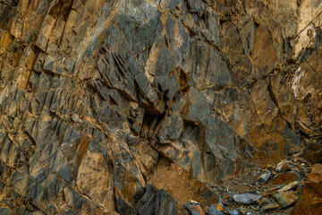Imposing rock formation stands tall in rugged mountainous landscape. Textured surfaces and coarse details create a dramatic atmosphere during daytime.