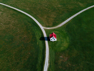 Aerial view of a small white house with a red roof at the intersection of two gravel paths on a green lawn. Symmetrical rural composition highlighting isolation and simplicity.