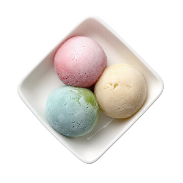 Three colorful, spherical desserts sit in a square, white dish, isolated on black