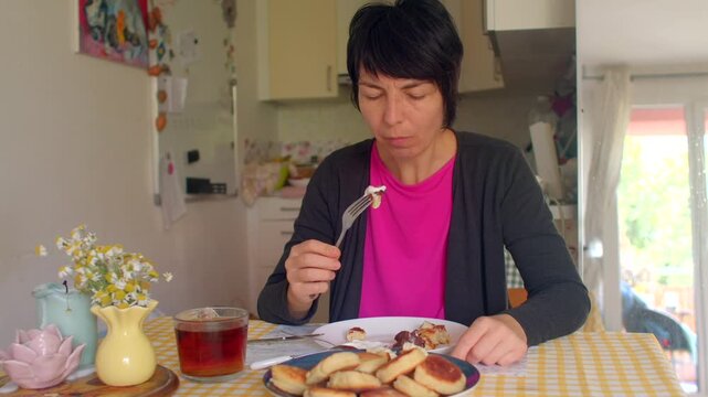 A woman enjoys a cozy meal, savoring pancakes and sipping tea. This scene captures the warmth of her contentment in a quiet moment - Powered by Adobe