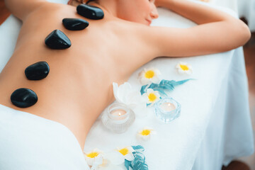 Hot stone massage at spa salon in luxury resort with day light serenity ambient, blissful woman customer enjoying spa basalt stone massage glide over body with soothing warmth. Quiescent