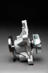 A new, shiny aluminum engine coolant pump on a gray gradient background. Contrast backlighting.