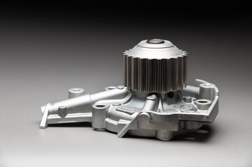 A new, shiny aluminum engine coolant pump on a gray gradient background. Contrast backlighting.