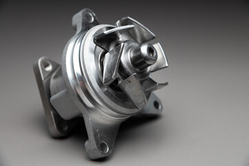 A new, shiny aluminum engine coolant pump on a gray gradient background. Contrast backlighting.