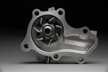 A new, shiny aluminum engine coolant pump on a gray gradient background. Contrast backlighting.