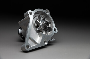 A new, shiny aluminum engine coolant pump on a gray gradient background. Contrast backlighting.