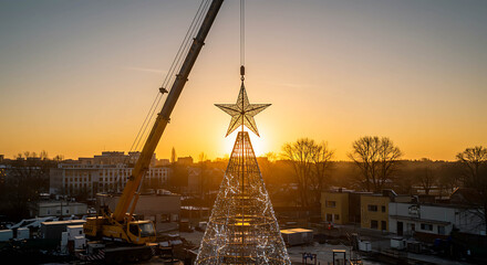 Crane placing star on top of Christmas tree at sunset  