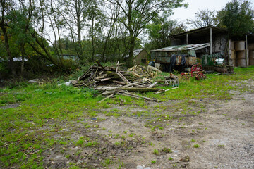 Rustic farmyard scene in Crich Derbyshire England with old farm machinery, wooden debris, a corrugated barn, and stacked hay bales under a grey sky.