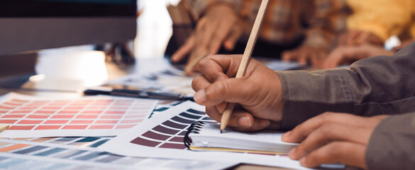 A group of diverse designers collaborates in a bright workspace, using color samples and sketching tools to brainstorm creative ideas and innovative projects. SACTR