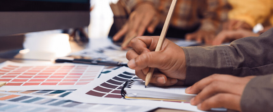 A group of diverse designers collaborates in a bright workspace, using color samples and sketching tools to brainstorm creative ideas and innovative projects. SACTR