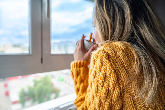 Woman drinking hot beverage contemplating view from window
