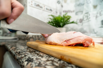 Cutting raw chicken breast on wooden board