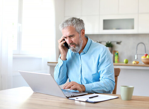 Portrait of a senior mature man or businessman working from home office using laptop and smart phone  at home