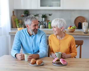 A man and a woman are smiling and holding cups of coffee in a kitchen. Scene is happy and friendly