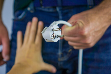 male hand holding a white european power plug extended toward a second outstretched hand against a man in blue jeans concept of male sexual health, energy transfer and connection, erectile dysfunction