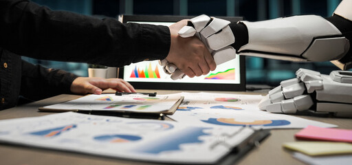 A human hand shakes a robot arm in a modern office, illustrating the partnership between technology...