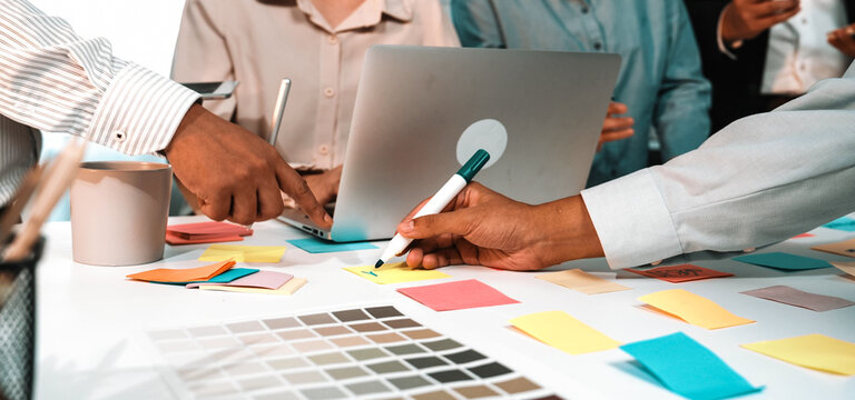 A diverse group of colleagues engages in a creative brainstorming session in a vibrant office. They utilize sticky notes and digital devices to refine their project ideas. SACTR - Powered by Adobe