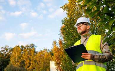 Inspector engineer using a tablet to take notes on a construction site. Male forestry studying the condition of trees in the forest. Work . Eco control. Ecologist conducting environmental monitoring.	
