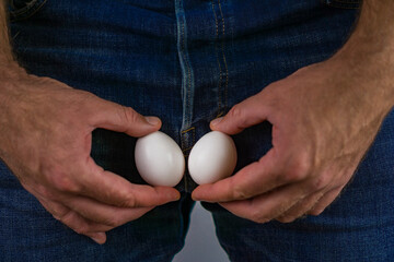male vasectomy and reproductive health, showing a man holding two eggs near jeans to represent fertility and sterilization.
