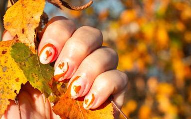female hands with orange beautiful manicure on the background of autumn leaves