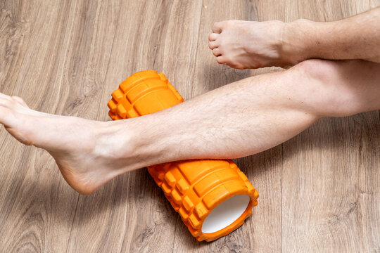 Athletic man using a foam roller to massage and relieve tension in his calf muscles after a demanding workout or training session. Post-exercise recovery, self-myofascial release, and self-care 