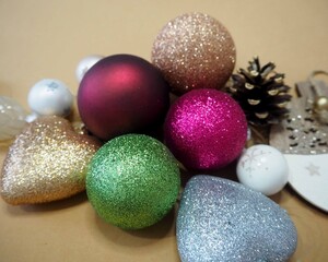 Glittering Christmas ornaments in various colors, including red, green, gold, blue, and pink, lying on a beige background with pine cone and festive decorations.