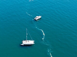 Aerial view of a small yacht and a sailboat sailing over the sea with turquoise water and shallow waves, luxury, lifestyle, ship, boat, cruise