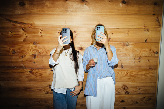 Female creators hiding faces playfully with their smartphones