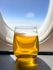 Close up view of a glass of lager beer in front of the window of a business class cabin of a passenger plane. no people.