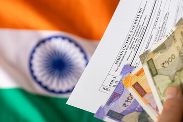 Indian taxes. A man holds an Indian income tax form and a rupee file in front of the Indian flag. The concept of financial settlement in India. Close up