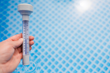 Person holding pool thermometer measuring water temperature