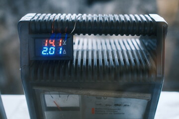 The digital display shows 14.1 volts and 2.0 amps on the dark battery charger.