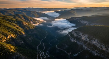 Aerial view of a winding road through a valley filled with low lying clouds