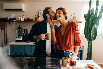 Couple in kitchen share a kiss and coffee