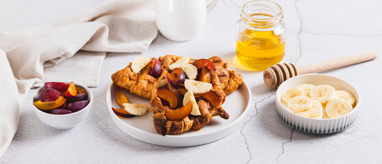 Sweet croffles with banana, plum and honey on a plate on the table web banner