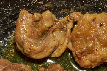 Pieces of chicken meat are fried in a frying pan, exuding flavor and mouth-watering appearance. Delicious chicken pieces are fried in a frying pan until golden brown.