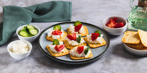 Appetizer of crackers with ricotta, cucumber and tomato on a plate on a table web banner