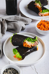 Rolls with tuna, Korean carrots, lettuce and sauce on a plate on the table vertical view