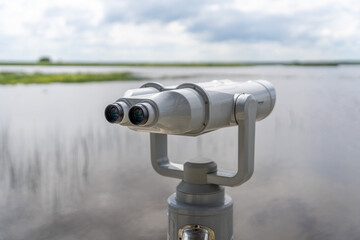 Fixed observation binoculars with a calm lake under a cloudy sky in background