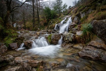 Obraz premium A serene mountain waterfall cascades over rugged rocks, showcasing nature's beauty. The gentle flow of water creates a tranquil atmosphere, inviting a sense of peace and relaxation.
