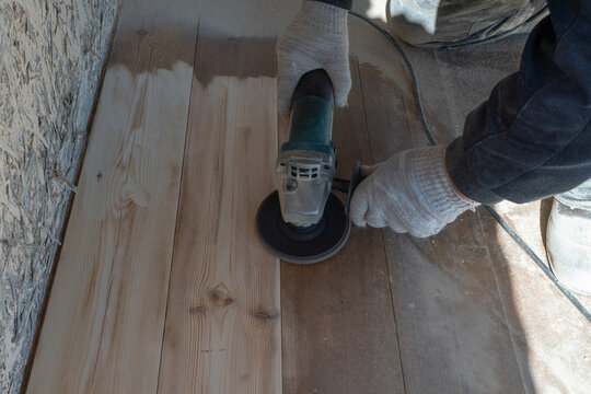 Wood floor sanding with electric sander by gloved worker in workshop