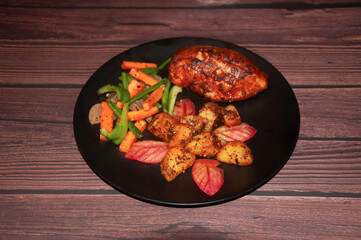 Gourmet Stuffed Chicken Breast with Roasted Potatoes and Sauteed Vegetables in black plate on wooden background top view